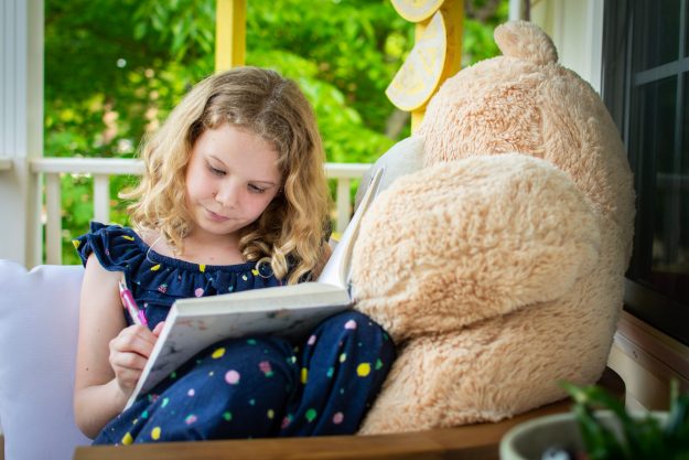 little girl writing with bear on side